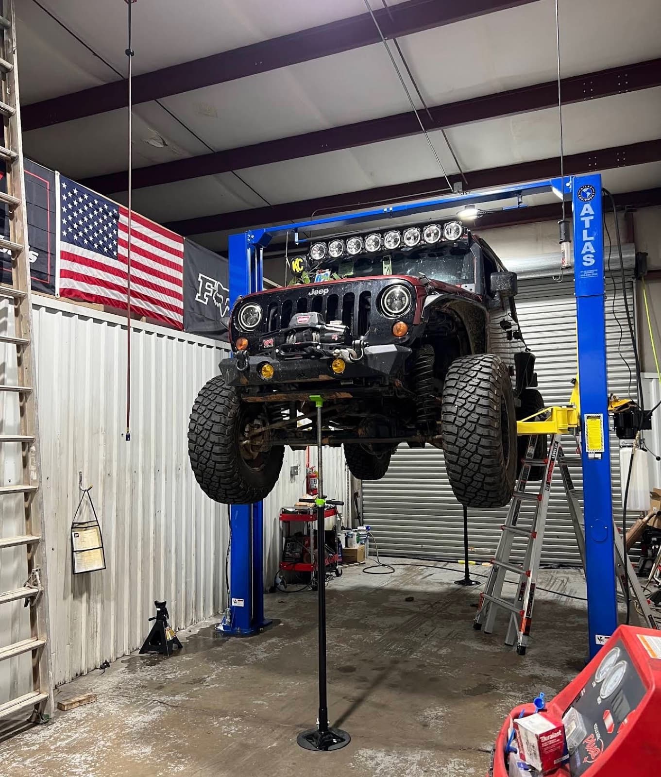 Red Jeep Wrangler JK raised on a two-post lift for suspension work inside the Tires To Go bay
