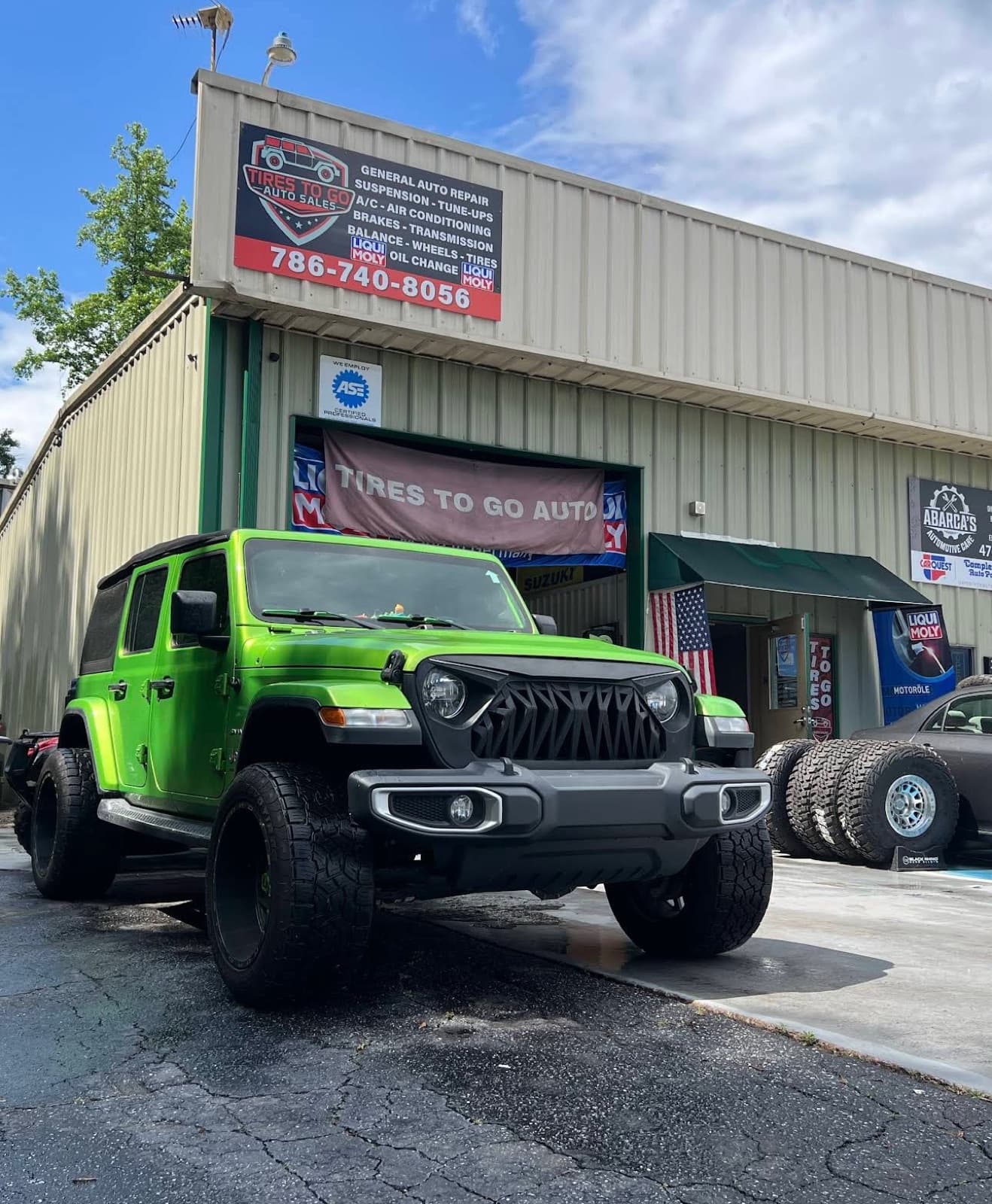 Custom green Jeep Wrangler with a lift and off-road grille parked in front of the Tires To Go storefront